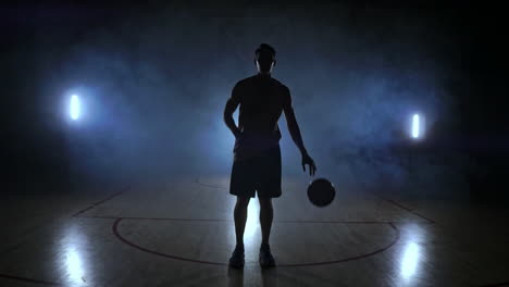 Der-Basketballspieler-Geht-Zur-Kamera-Und-Wirft-Den-Ball-Auf-Den-Boden.-Dann-Bleibt-Er-Stehen,-Hält-Den-Ball-Und-Blickt-In-Die-Kamera